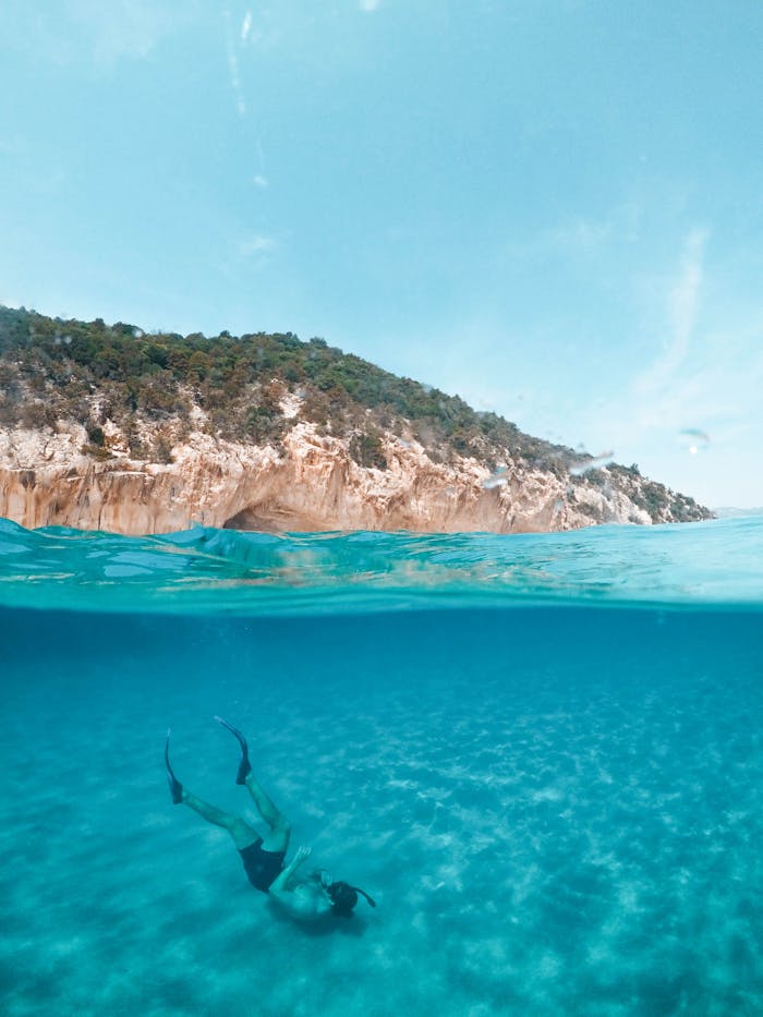 A serene over-under photograph capturing a diver exploring the turquoise waters off the coast of Sardinia, Italy.