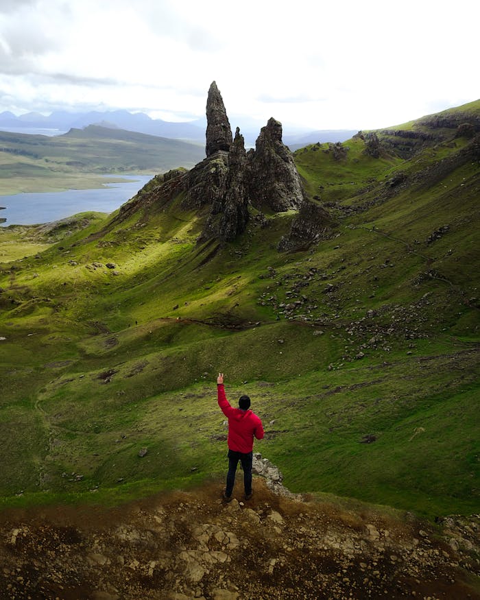 brand-02 A lone hiker in a red jacket stands before the iconic Old Man of Storr on the Isle of Skye, Scotland.