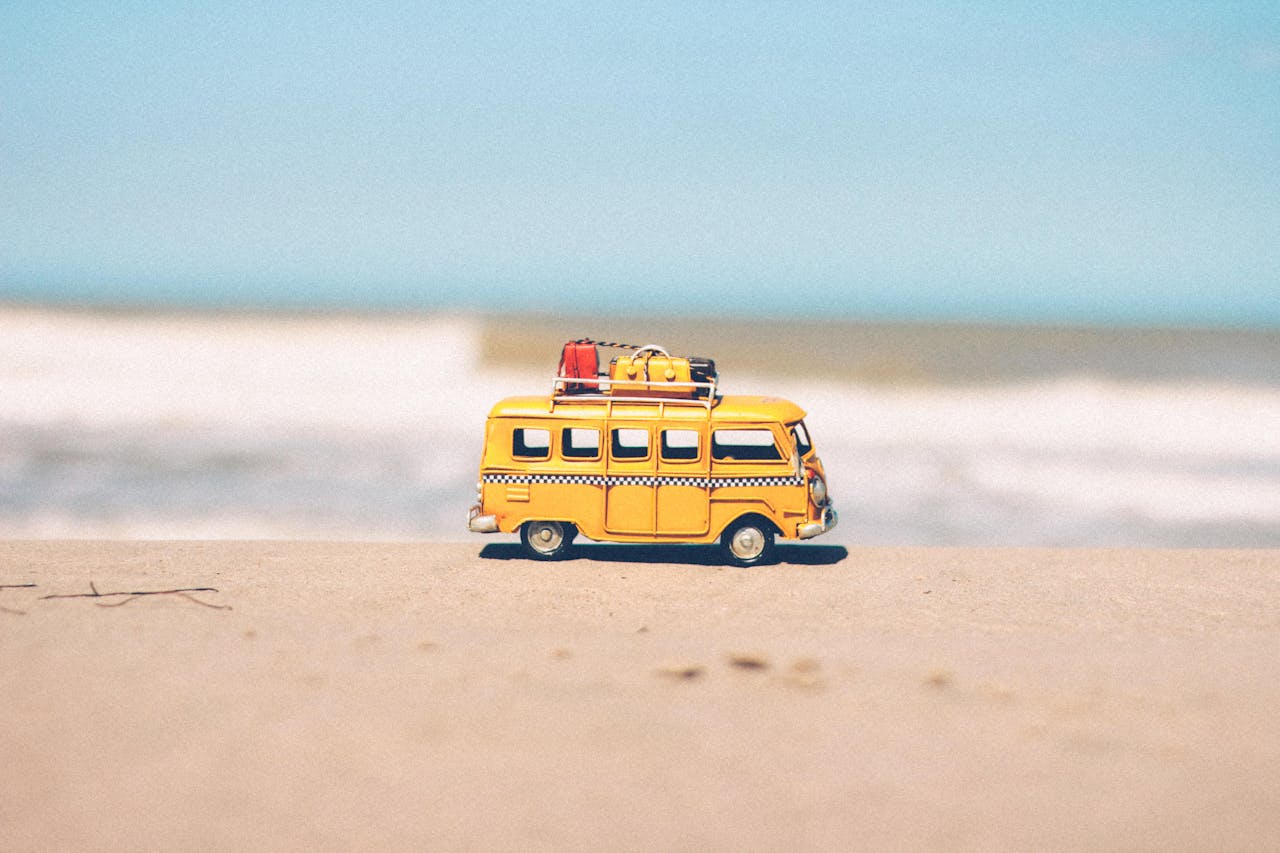 mobile-02 A vibrant yellow toy van sits on a sandy beach with an ocean backdrop, symbolizing fun travel adventures.